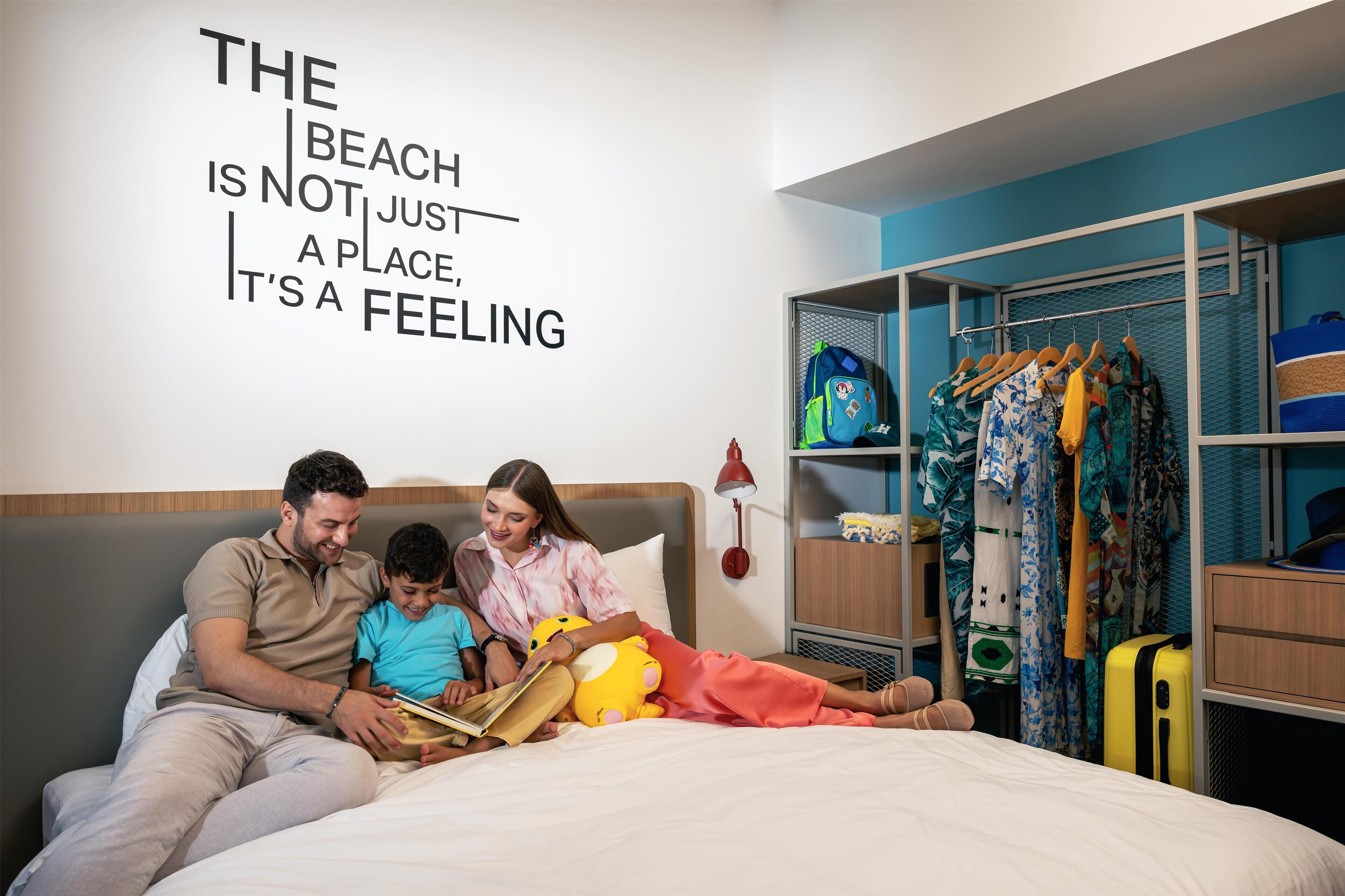 A hotel room with a bed, a wall with a motivational quote, a wardrobe, and a suitcase.