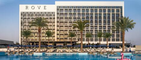 A hotel with a pool area, featuring lounge chairs and umbrellas, and a prominent building with the name 'ROVE'.