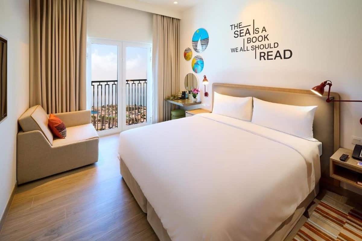 Habitación de hotel con una cama grande, un sofá, un escritorio y un balcón con vistas.