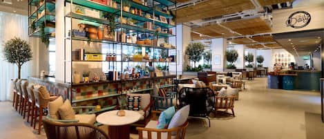 A modern interior with a central shelving unit displaying various decorative items, surrounded by seating areas with wicker chairs and a round table.