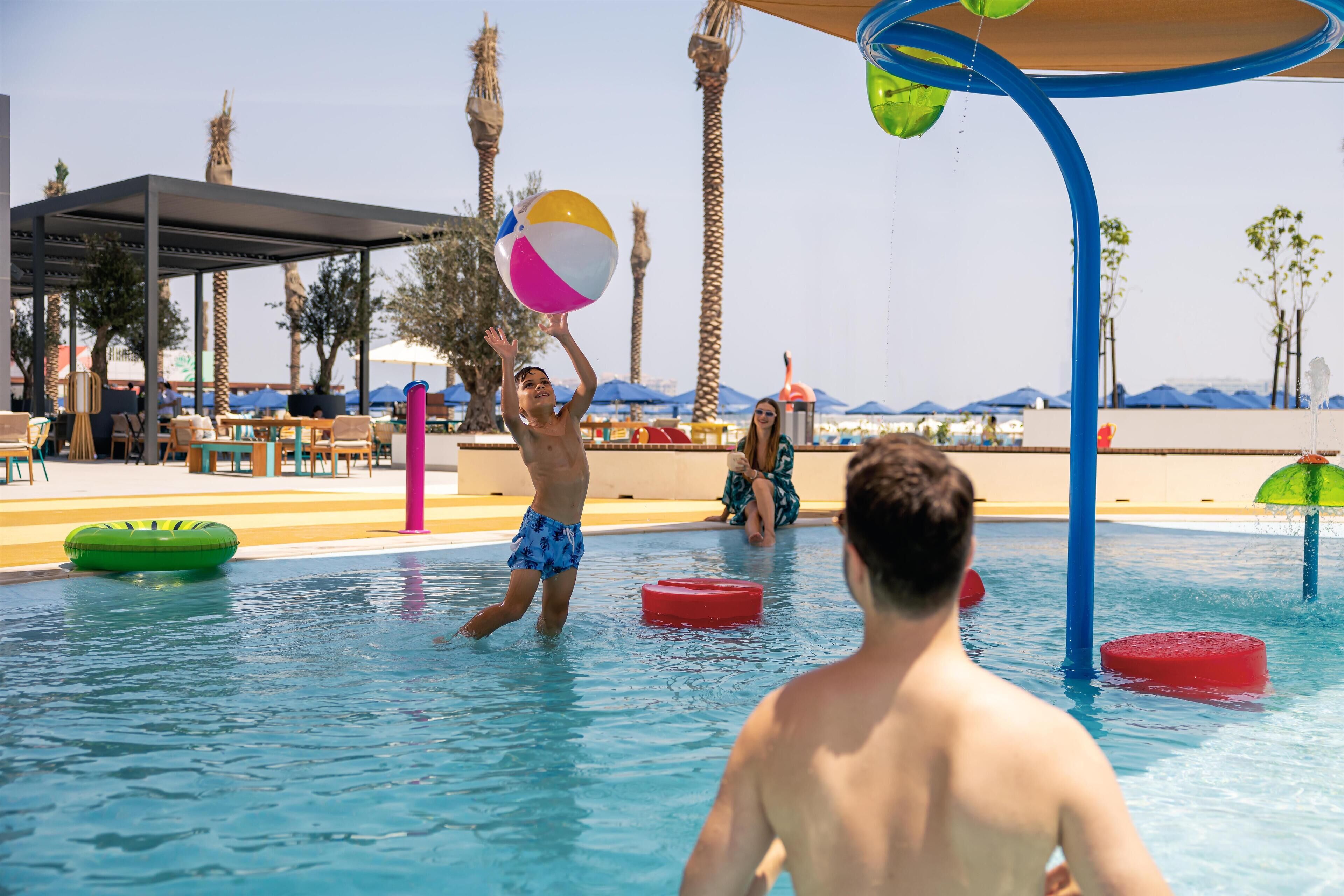 Área de piscina com estrutura de recreação aquática, cadeiras de descanso e palmeiras.