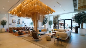 A modern hotel lobby with a large wooden ceiling installation, comfortable seating areas, and large windows offering views of the outdoors. - Rove Al Marjan Island (Ras Al Khaimah)