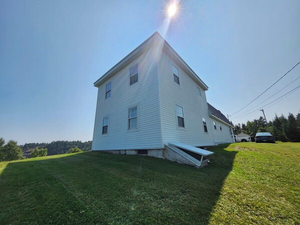 A two-story white building with a sloped roof, a small porch, and a grassy yard.