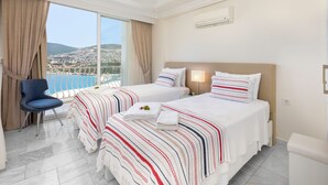 Habitación de hotel con dos camas, un ventanal con vistas a la costa, un ventilador de techo y un equipo de aire acondicionado.