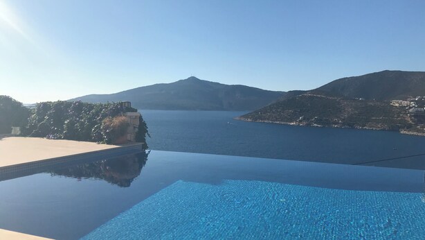 Vista despejada de una piscina con borde de azulejos, rodeada por un paisaje natural con colinas y una masa de agua.