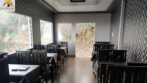 Un restaurant avec des tables et des chaises en bois, un papier peint à motifs et de grandes fenêtres donnant sur l’extérieur.