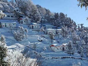 A snow-covered village with several small buildings, likely guest houses or cottages, arranged on a hillside. - Dev Bhoomi Resort (Tehri)