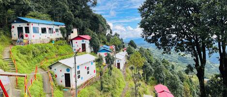 A hillside with several small buildings, some with red roofs, surrounded by lush greenery and a clear sky.