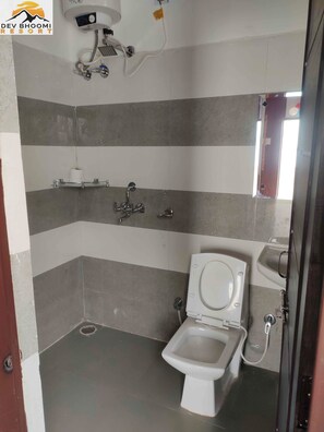 A small, tiled bathroom with a toilet, a hand dryer, and a towel dispenser. - Dev Bhoomi Resort (Tehri)
