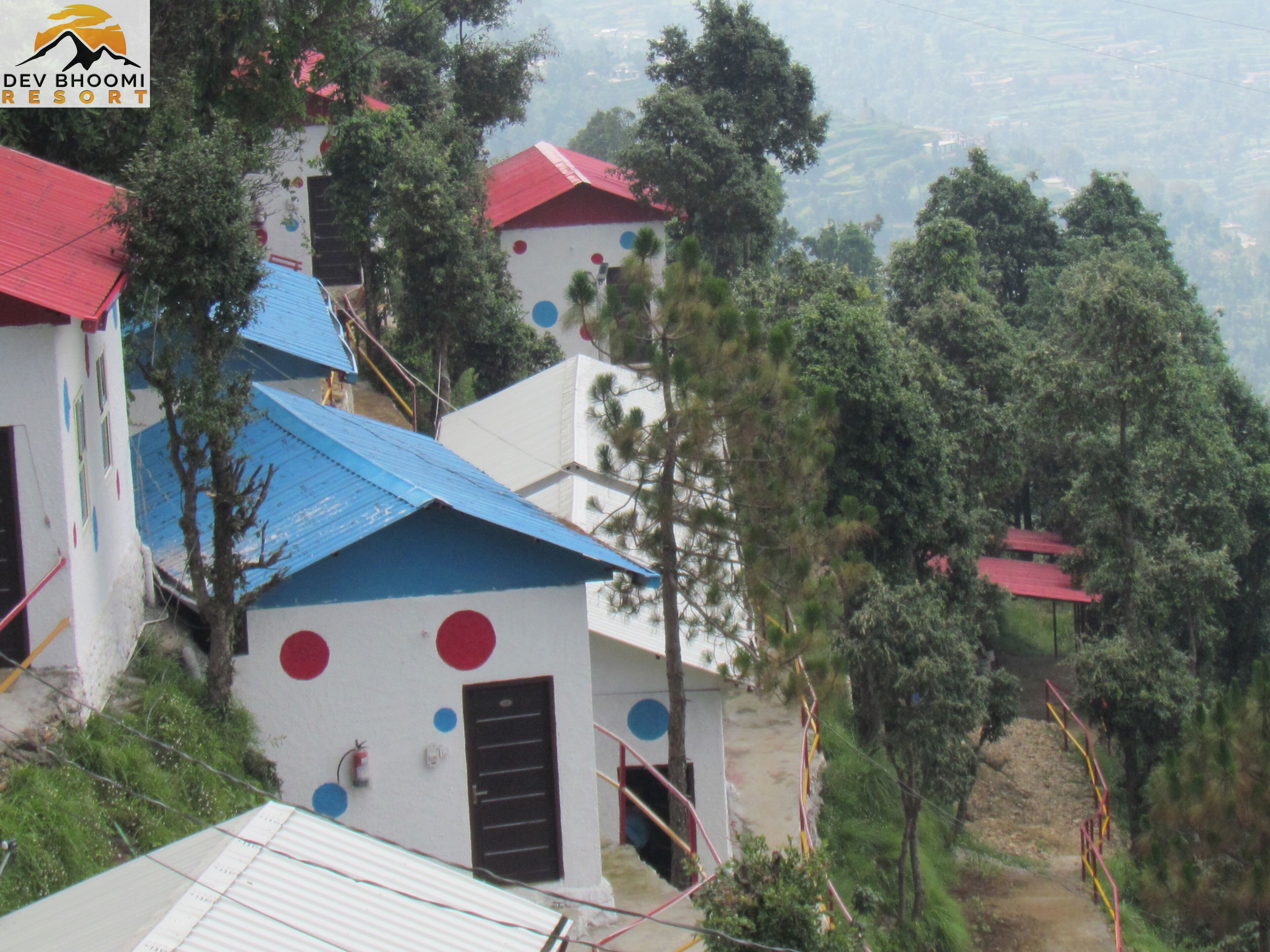 Un complejo turístico en una ladera con edificios de colores, un sendero de tierra y abundante vegetación.