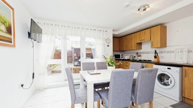 Een moderne keuken met houten kastjes, een wasmachine en een eethoek met een tafel en stoelen.