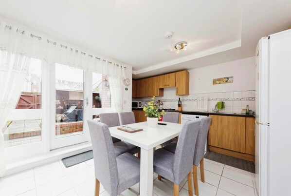 Une cuisine moderne avec des meubles en bois, un plan de travail blanc et un coin repas comprenant une table blanche et des chaises grises.