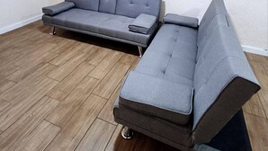 Ein Zimmer mit einem grauen Modulsessel, einem Flachbildfernseher an der Wand und Holzboden.