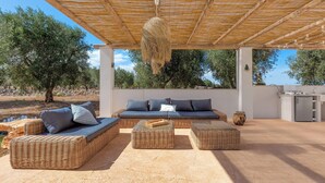 Un espace extérieur aménagé avec des meubles en osier, une terrasse couverte et une vue sur les oliviers.
