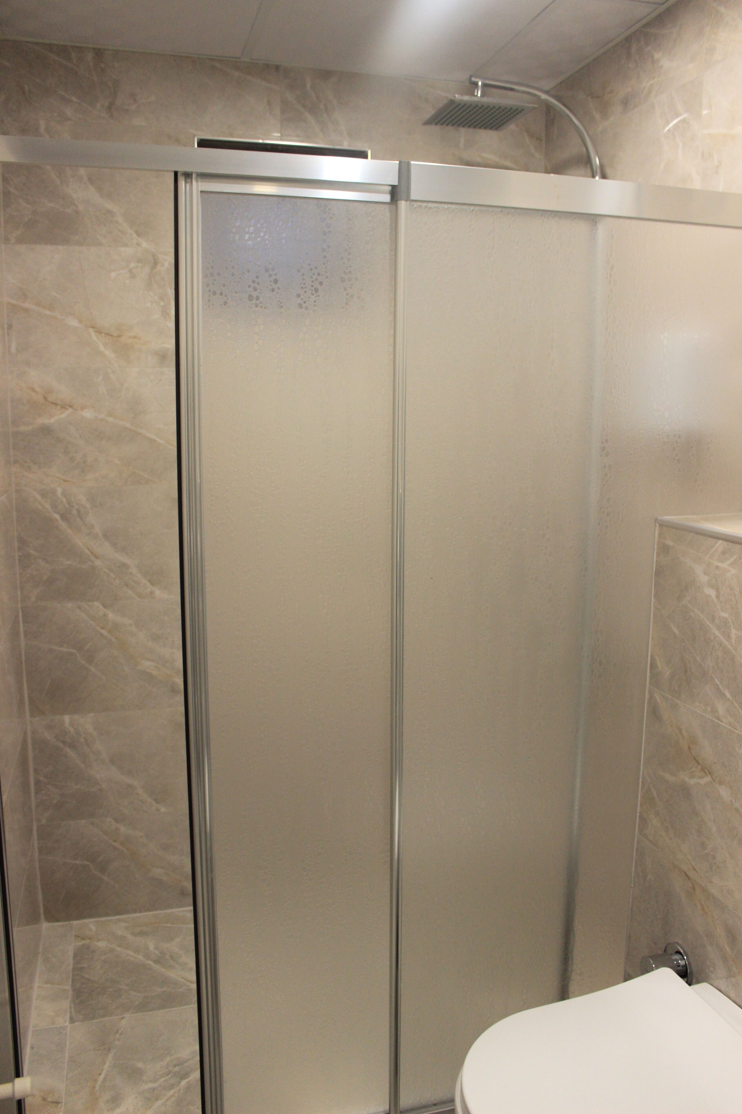 A bathroom with a glass-enclosed shower, a white toilet, and marble walls.