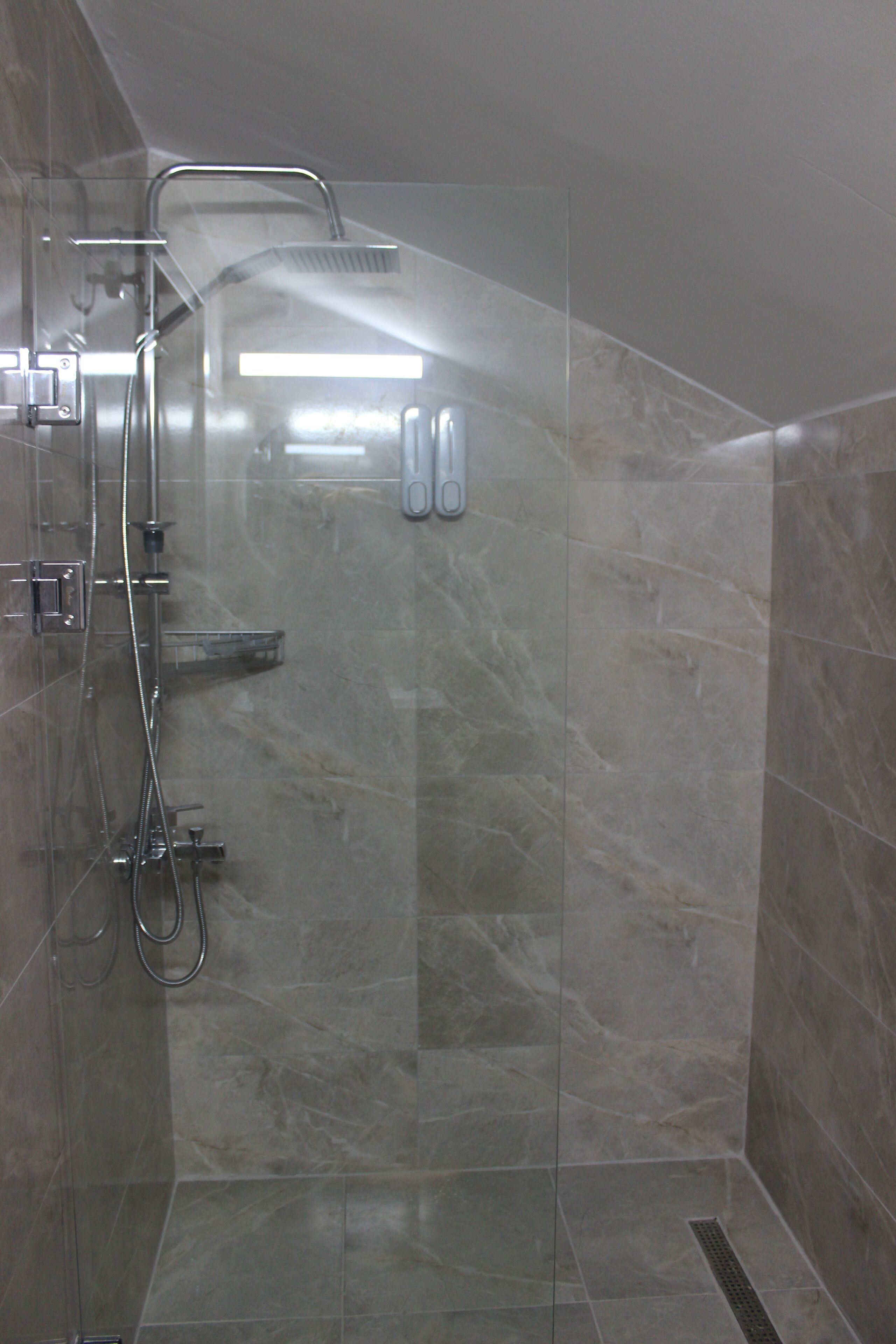 A glass-enclosed shower stall with a handheld showerhead, a handheld shower attachment, and a wall-mounted faucet.