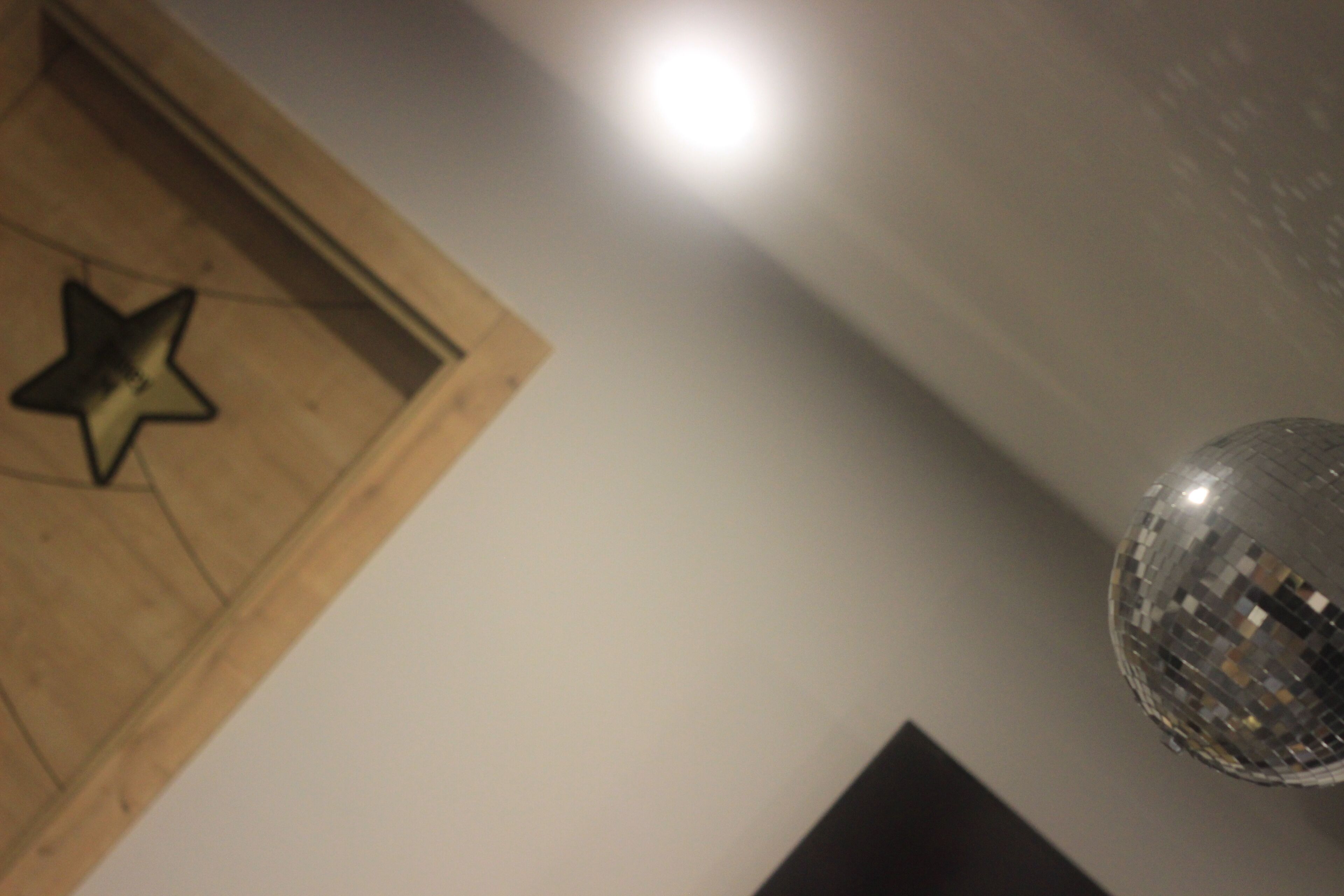 Un adorno con forma de estrella de madera en una pared, una bola de discoteca y un objeto rectangular oscuro.