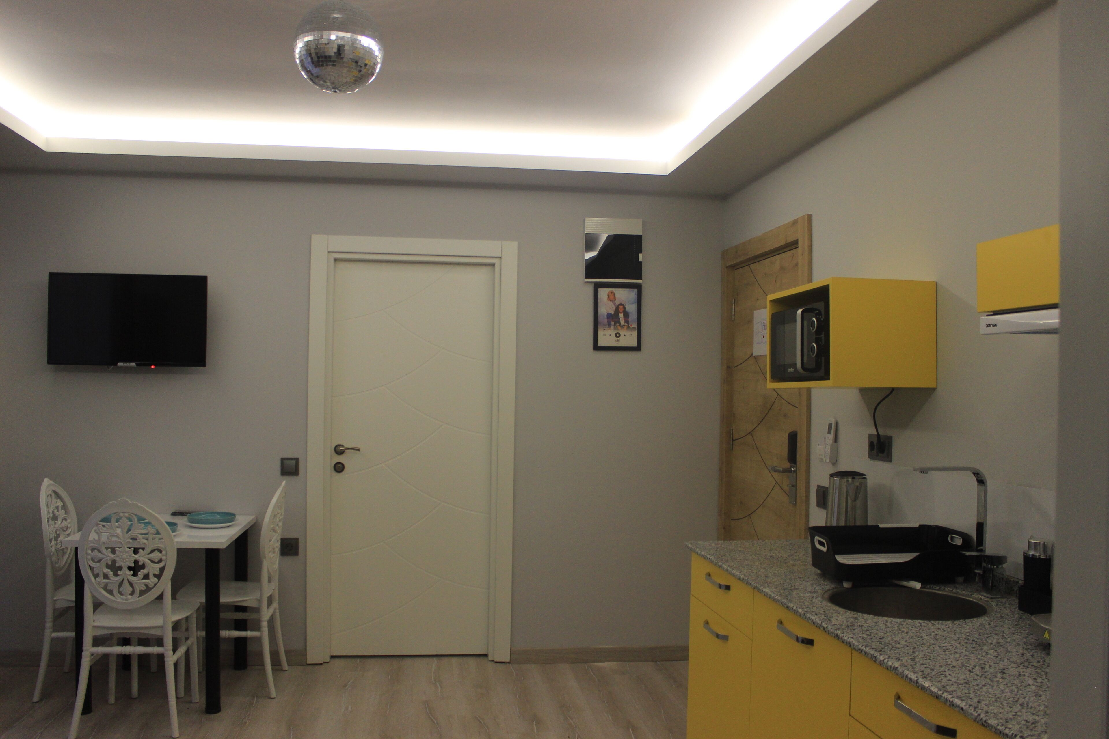 A compact kitchen with a microwave, sink, and a flat-screen TV mounted on the wall.