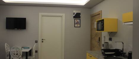A compact kitchen with a microwave, sink, and a flat-screen TV mounted on the wall.