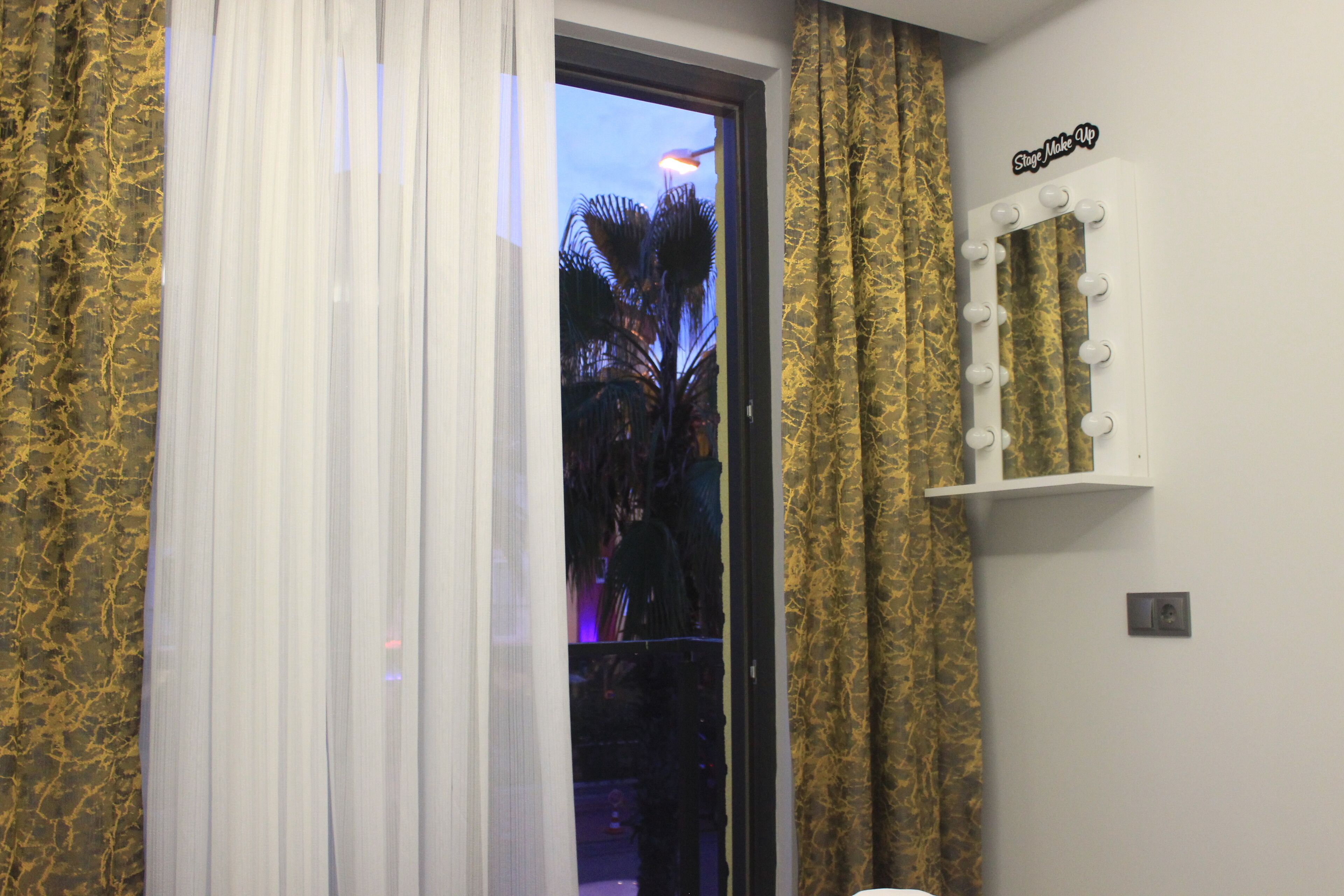 A room with a window, curtains, a vanity with lights, and a sign that reads "Stage Make Up".