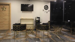 A modern lounge area with a flat-screen TV, a coffee machine, and a 'Music Please' sign.