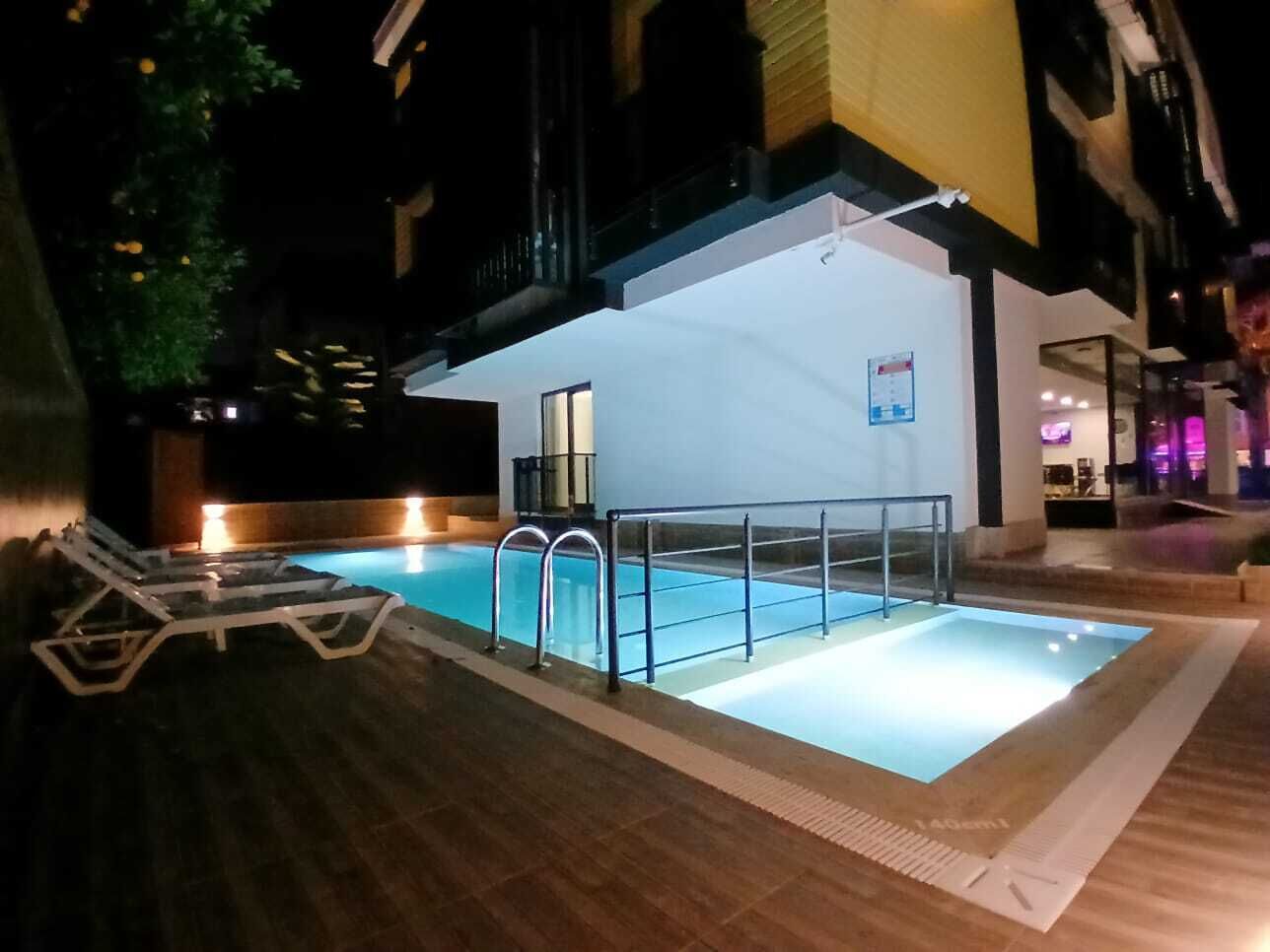 Una piscina interior con barrera de vidrio, sillas de descanso y suelo de baldosas.