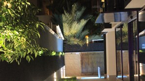 A nighttime outdoor area with a pathway, illuminated grass, and a building with glass doors.