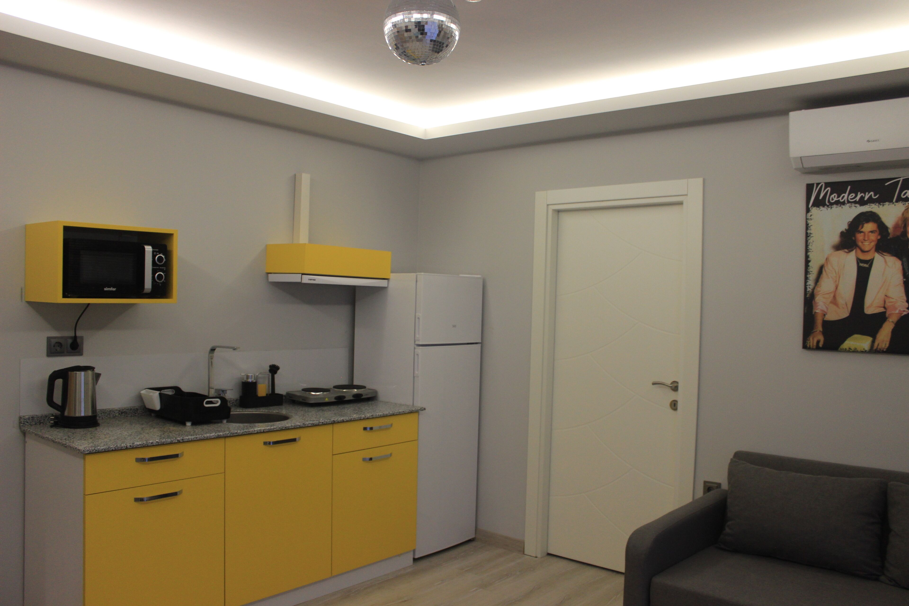A compact kitchen with yellow cabinets, a microwave, a refrigerator, and a small dining area with a couch.