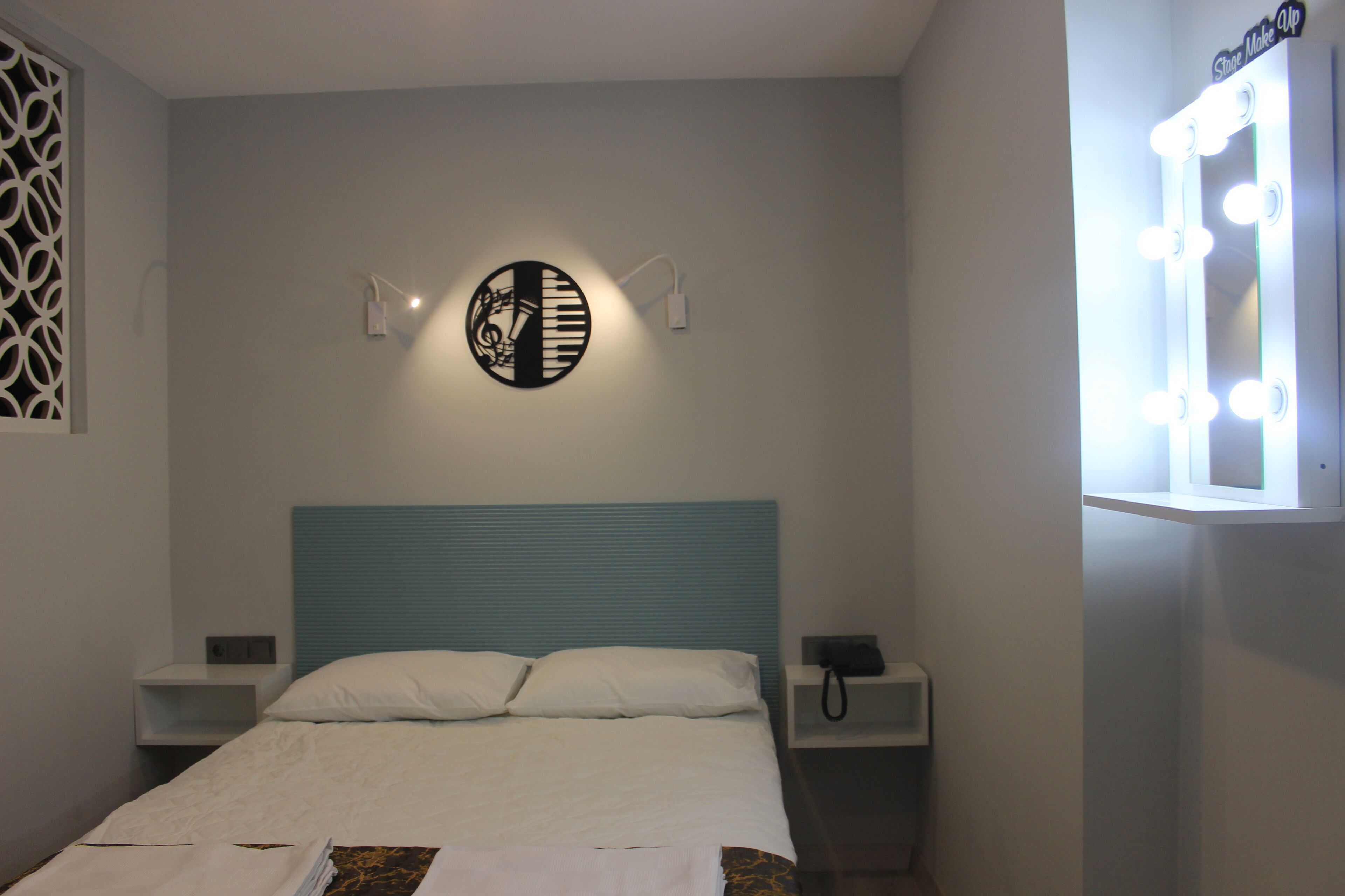 Ein Hotelzimmer mit einem Bett, Nachttischen, einer Wanduhr und einem beleuchteten Spiegel.