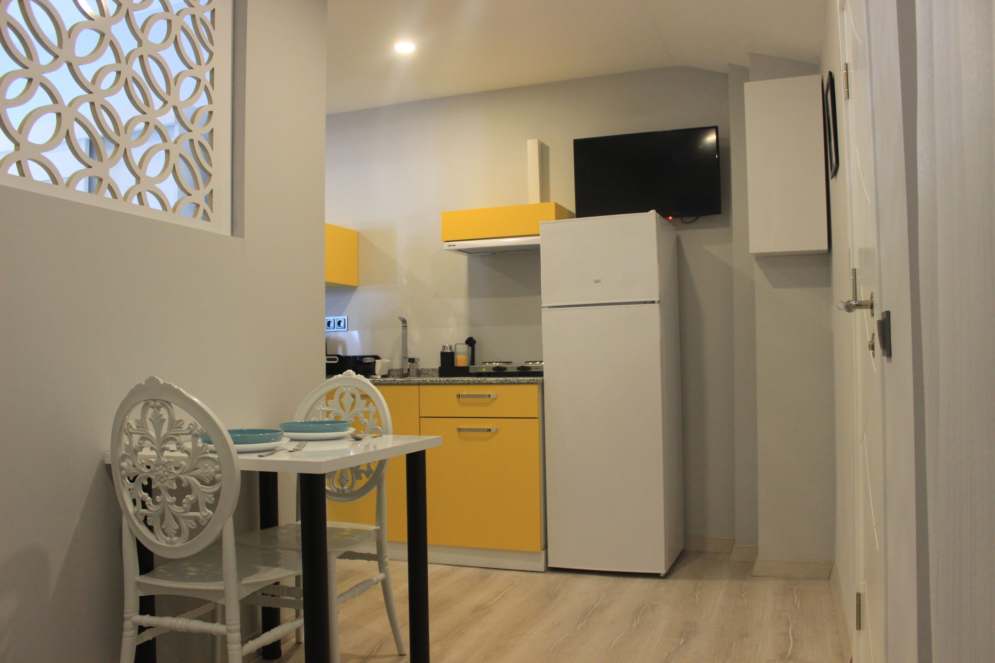 A compact kitchen with a white refrigerator, yellow cabinets, and a flat-screen TV mounted above the counter.