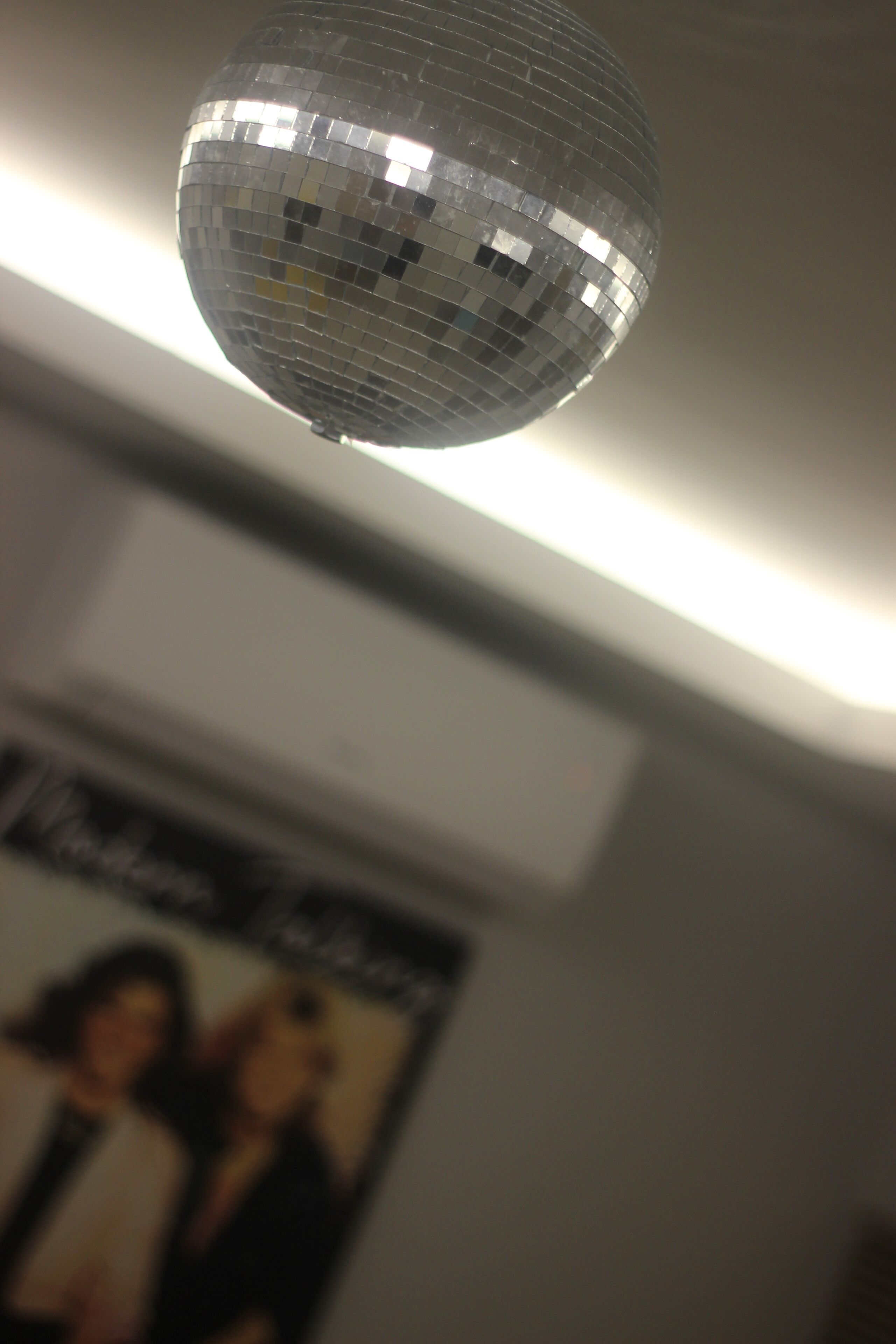 Een discobal hangt aan het plafond in een kamer met een poster aan de muur.
