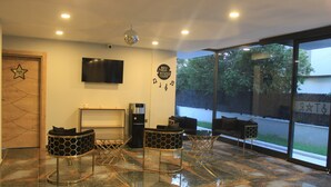 A modern lobby with a glass door, a mounted TV, and hexagonal patterned chairs.