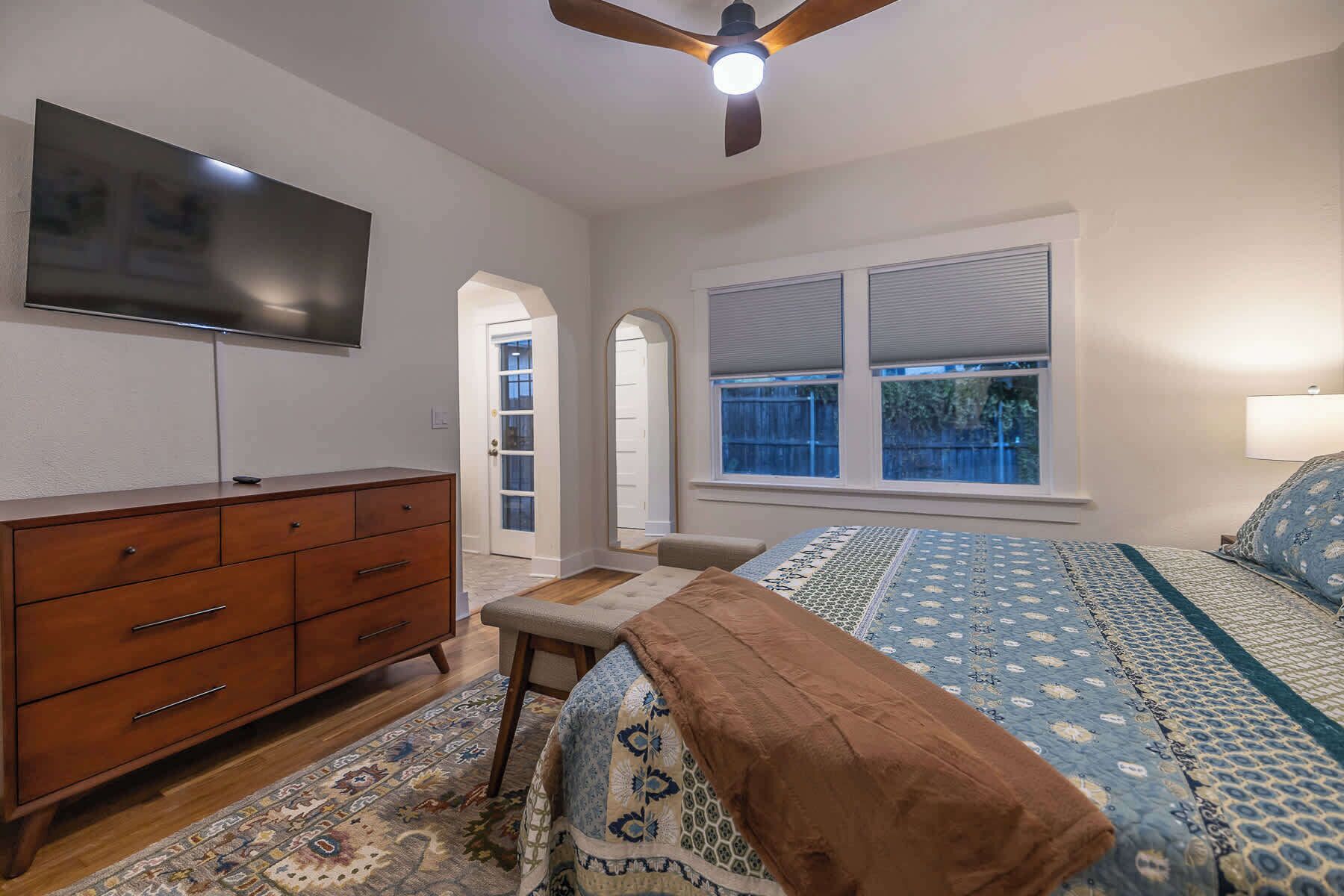 A bedroom with a bed, a dresser, a television, and a ceiling fan.