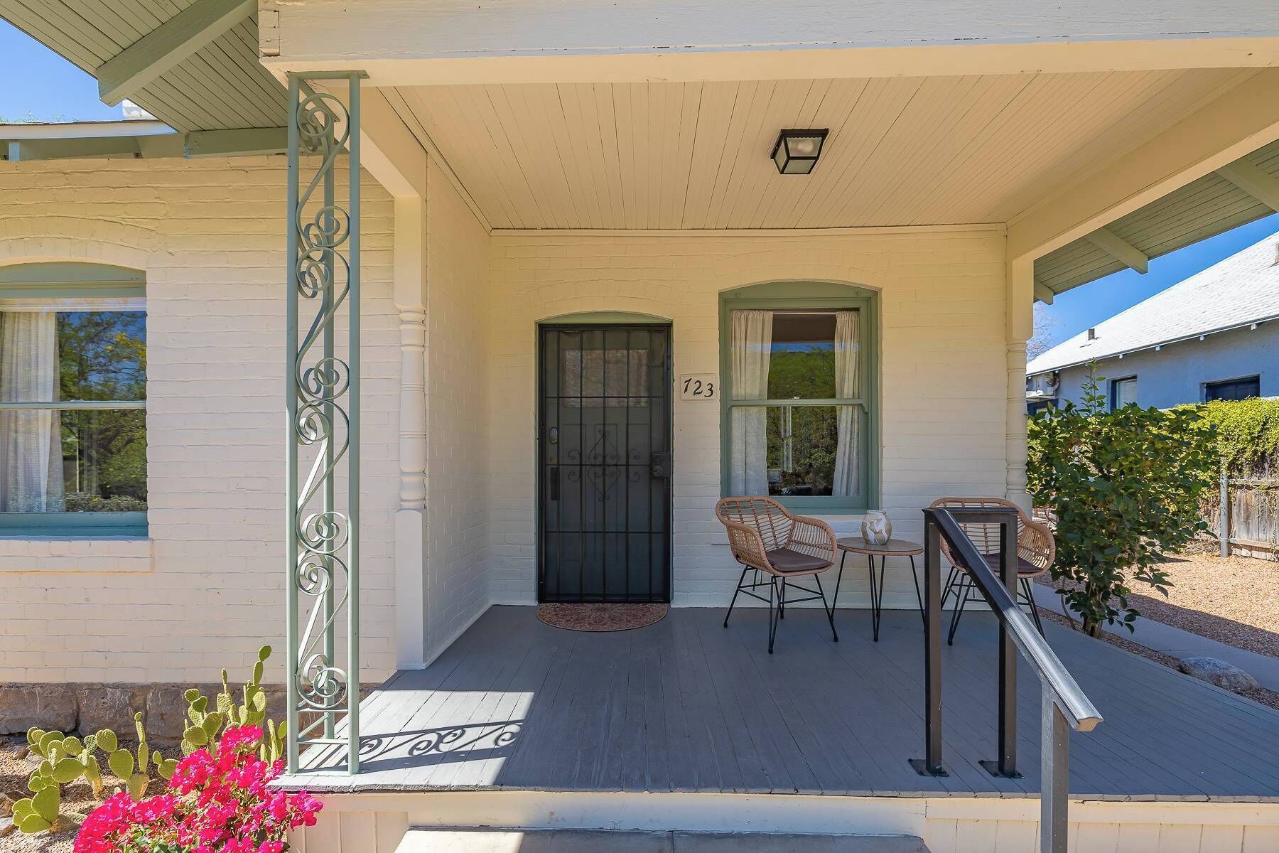 A house with a porch, a black door, and two windows with green frames.