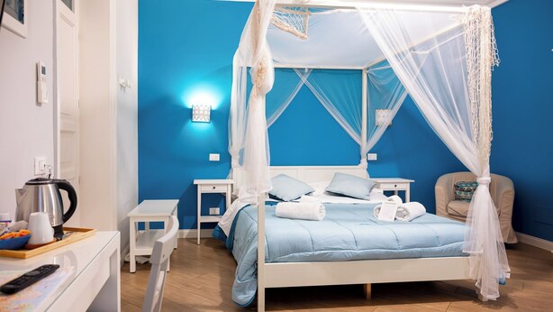 A bedroom with a four-poster canopy bed, bedside tables, a chair, and a small table with a kettle and cups. - Palazzo Carella (Palermo)