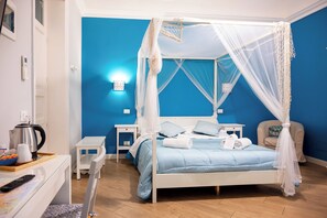 Un dormitorio con cama de dos plazas con dosel, mesitas de noche, una silla y una pequeña mesa con hervidor y tazas.