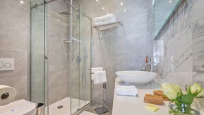 Un baño moderno con ducha envuelta en cristal, un lavabo grande de color blanco y una pared revestida de mármol.