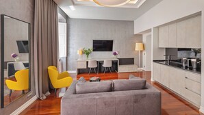 Una sala de estar moderna con un sofá gris, sillas amarillas, un televisor de pantalla plana y una zona de comedor con una mesa y sillas blancas.