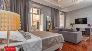 Un dormitorio moderno con una cama grande, un sofá gris, un televisor y un balcón con vistas.