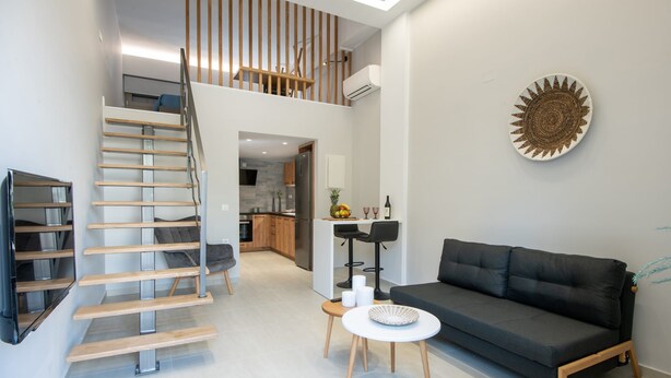 Un espace de vie moderne comprenant un escalier, un canapé, une petite table et un coin cuisine à l’arrière-plan.