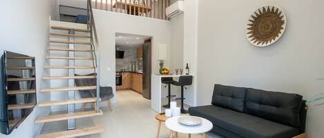 Un espacio de estar moderno con una escalera, un sofá, una mesita y una cocina al fondo.