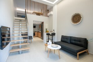 A modern living space with a staircase, a sofa, a small table, and a kitchen area in the background.