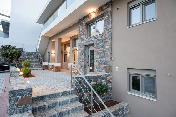 A modern building with a stone facade, a staircase leading to a covered entrance, and outdoor seating.