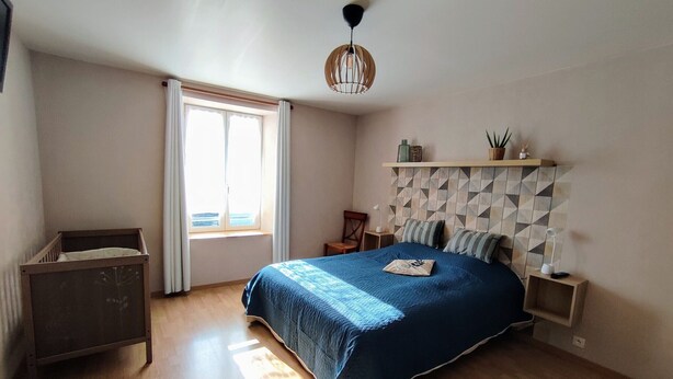 A bedroom with a bed, a nightstand, a chair, a window with curtains, and a hanging light fixture. - Comfortable cottage with fireplace and parking, near Verdun (Dompcevrin)