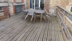 A wooden deck with a table and chairs, a sliding glass door, and a brick wall. - Comfortable cottage with fireplace and parking, near Verdun (Dompcevrin)