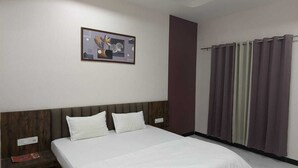 A hotel room with a bed, a ceiling fan, a wall-mounted air conditioner, a window with curtains, and a framed picture on the wall. - Hotel Dhruvnanda Palace Khategaon (Khategaon)