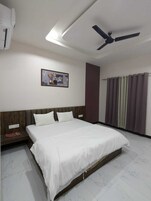 Quarto de hotel com cama, ventoinha no teto, ar condicionado fixado na parede, janela com cortinas e um quadro emoldurado na parede.