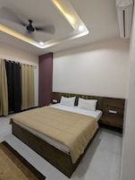 Quarto de hotel moderno com uma cama grande, ventilador de teto, iluminação embutida e ar condicionado.