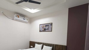 A bedroom with a bed, a ceiling fan, an air conditioner, a framed picture on the wall, and a wooden nightstand. - Hotel Dhruvnanda Palace Khategaon (Khategaon)
