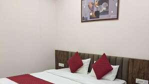 A neatly made bed with a red and white bedspread, a wooden headboard, and a single bedside table with a lamp. - Hotel Dhruvnanda Palace Khategaon (Khategaon)